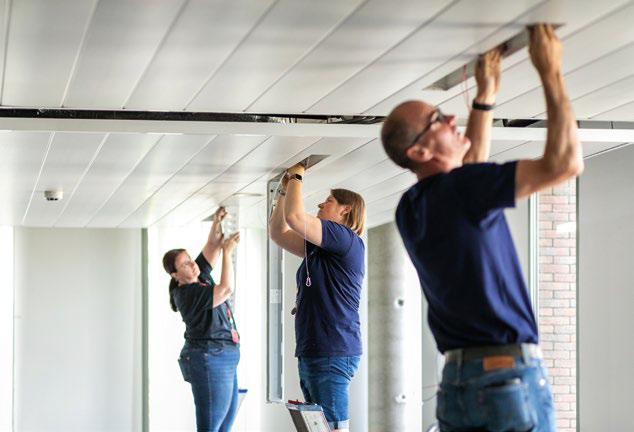 Photo de trois personnes intervenant sur des luminaires au plafond. Dossier Réparabilité.